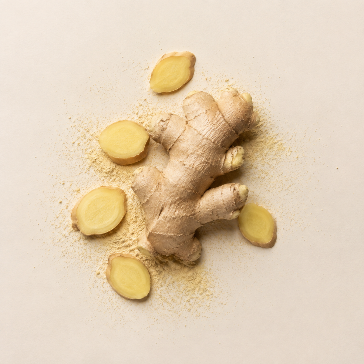 A whole ginger root with several sliced pieces and a light dusting of powder, arranged on a plain light beige background. Image